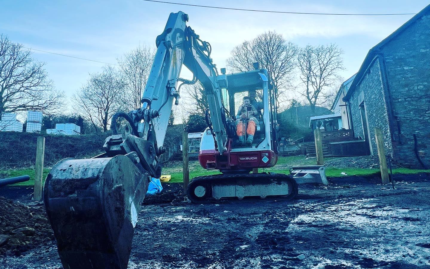 A red and white Takeuchi digger parked on a muddy construction site during groundworks.