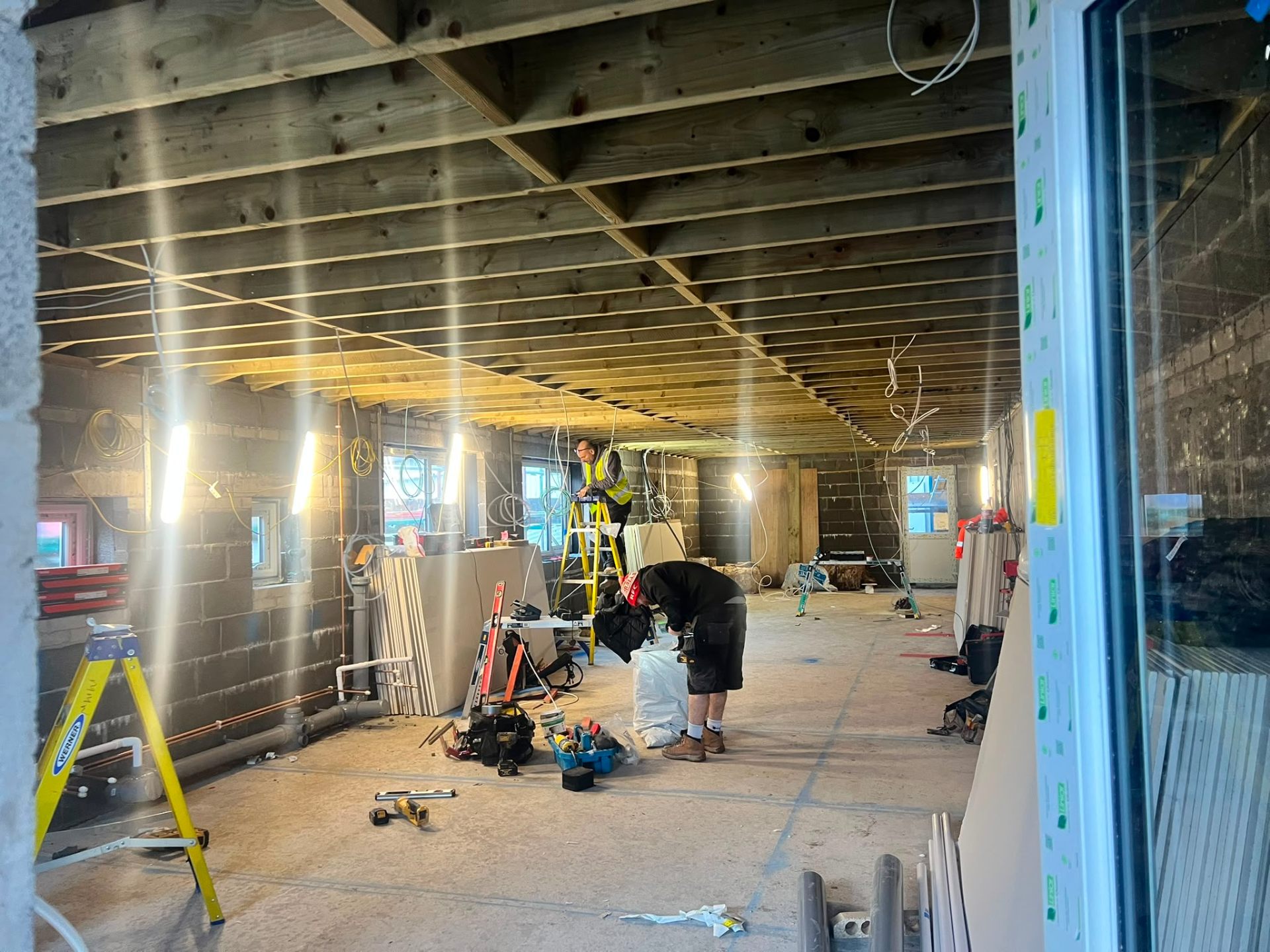 Large interior extension project showing exposed ceiling joists, blockwork walls, and electrical wiring work.