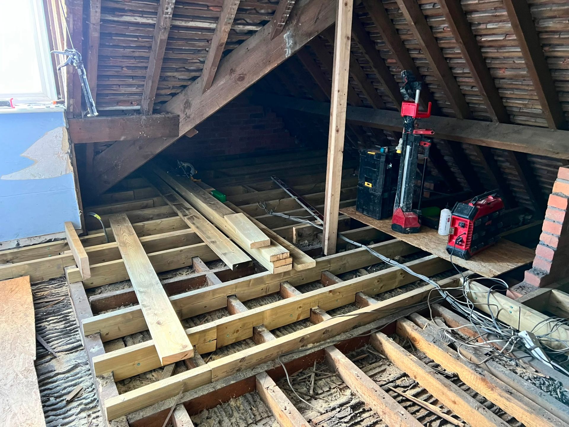 Loft conversion interior showing timber joists, construction tools, and roof rafters during development.