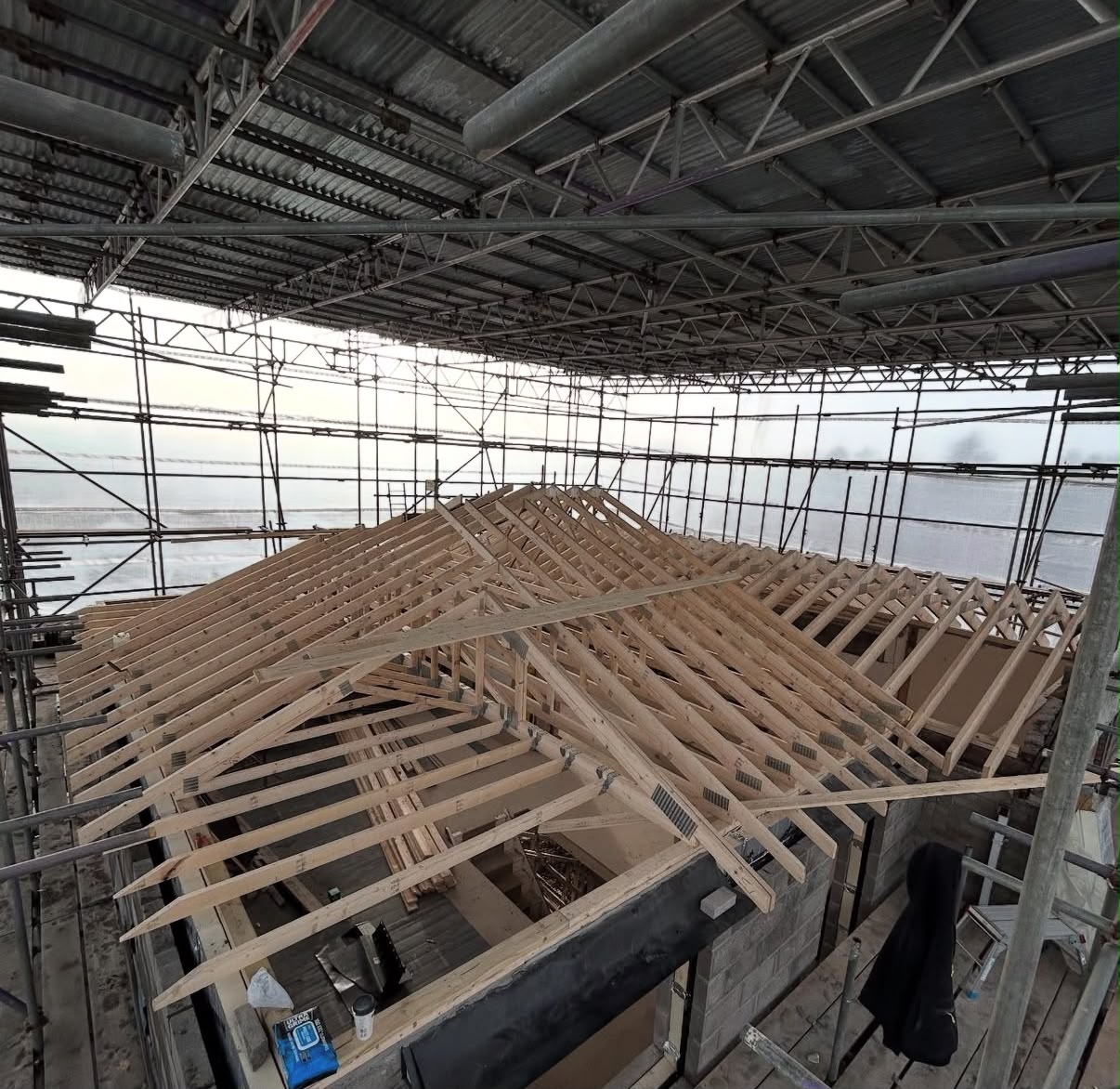 Structural timber roof trusses installed on a new build masonry shell under protective site scaffolding.