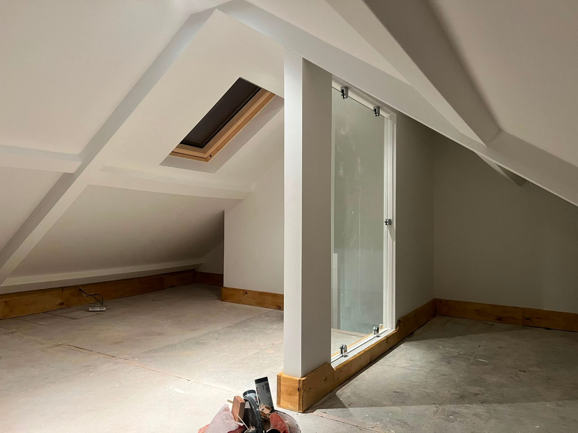 Loft conversion in progress with freshly plastered sloped ceilings, Velux skylight and glass balustrade landing by LEWZ Property Development