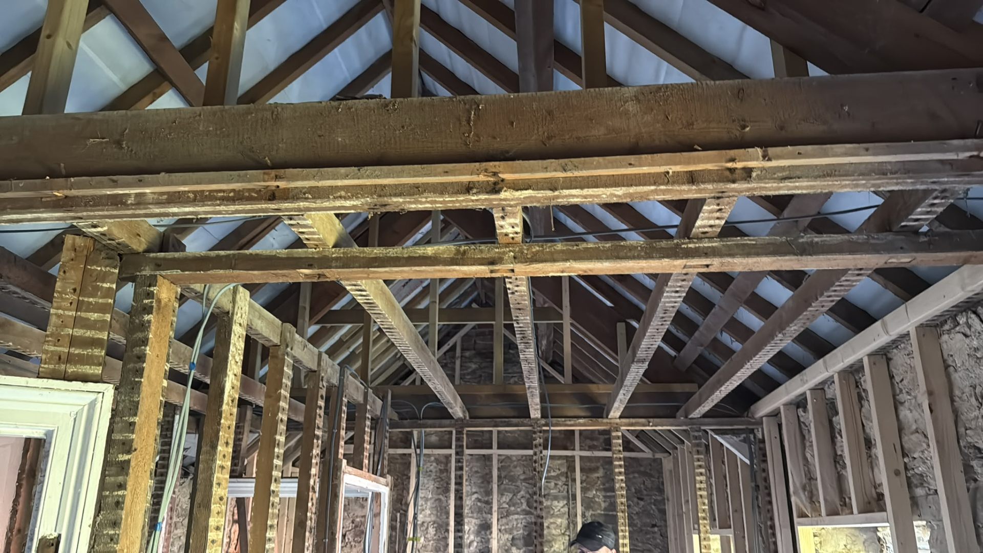 Internal view of exposed timber roof trusses and wall stud framing mid-construction in a house extension.