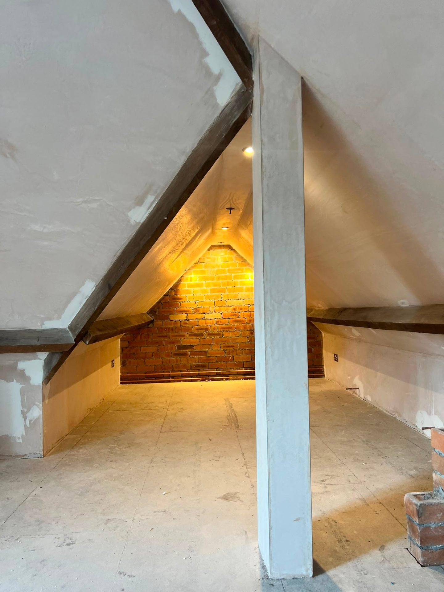 Loft conversion under construction showing fresh plaster and an illuminated exposed brick feature wall.