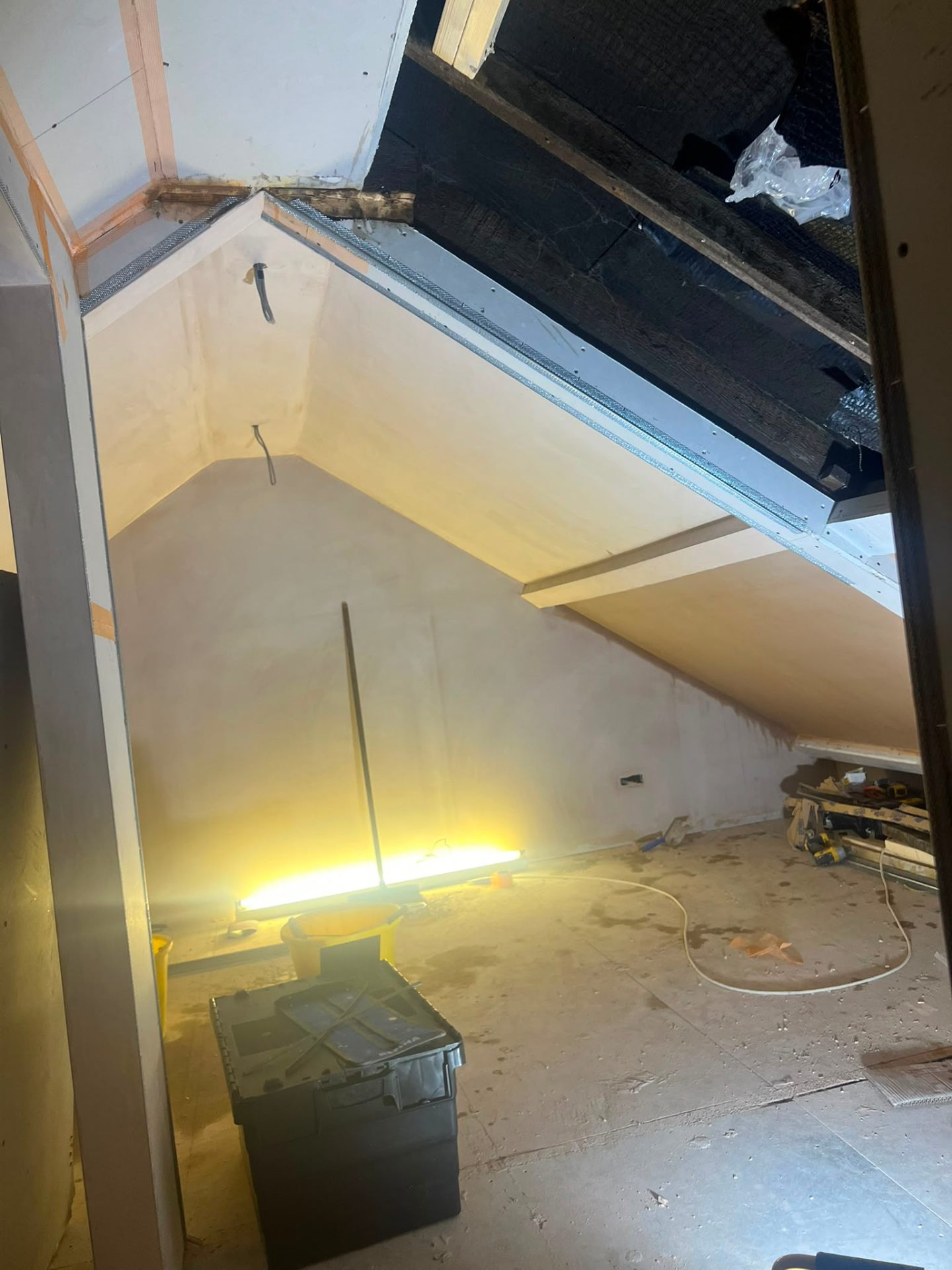 An attic loft conversion in progress showing plastered walls and exposed roof timber beams.