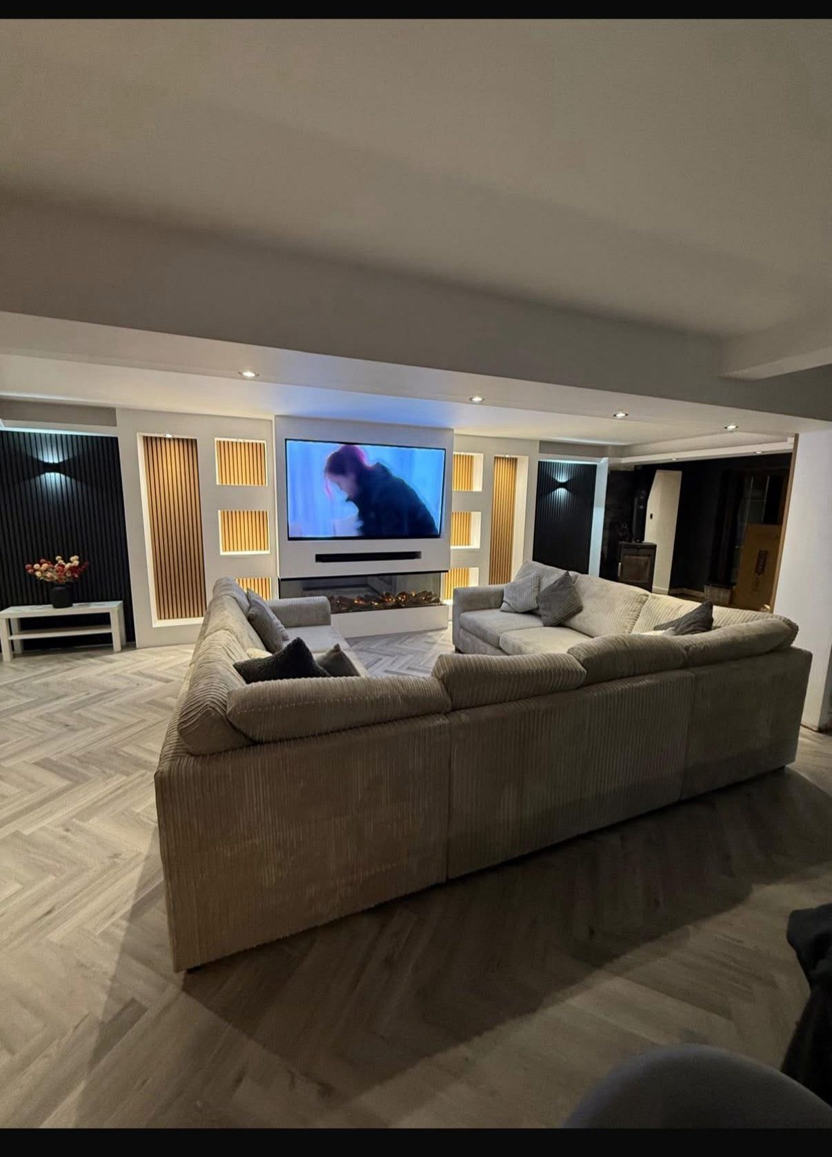 Bespoke media wall with recessed TV, slim inset fireplace and slatted timber feature panels with integrated lighting in a contemporary living room by LEWZ Property Development