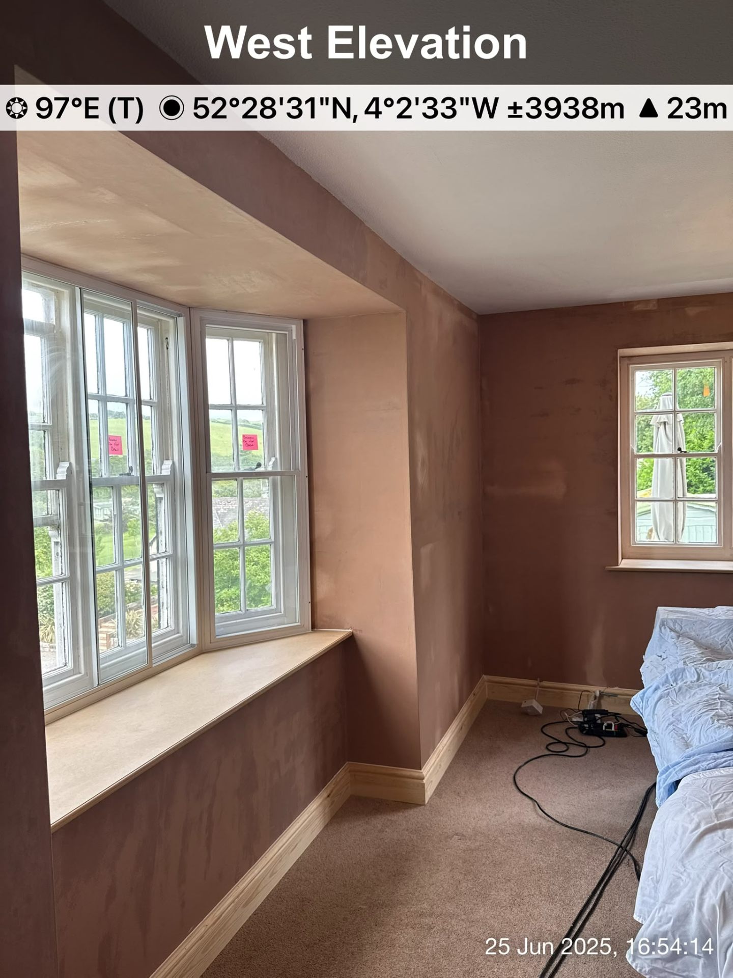 A bedroom renovation showing freshly plastered walls around a large bay window and smaller side window.