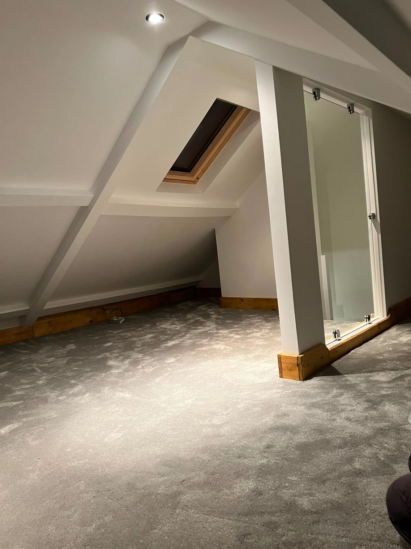 Completed attic room renovation with grey carpet, glass balustrade, and integrated spotlighting.