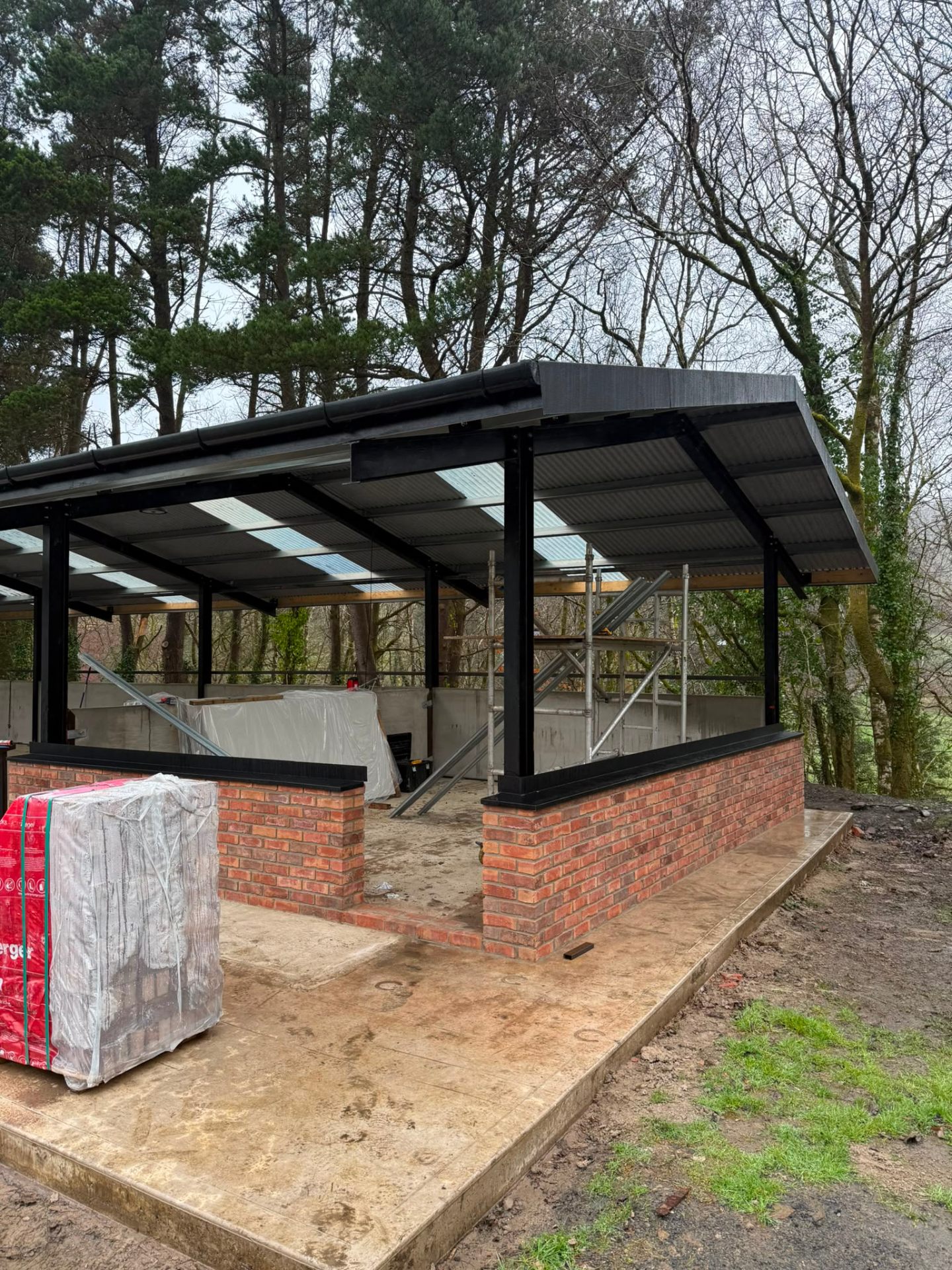 Progress of a timber and steel frame outdoor structure with red brick foundation walls.