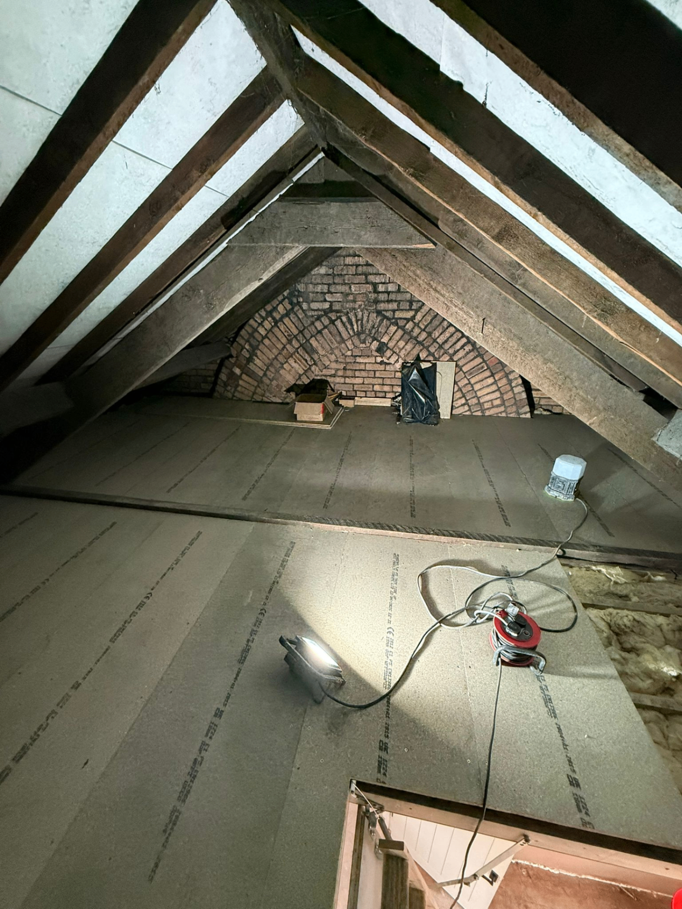 Attic conversion in progress with insulated boarding to sloped ceilings, exposed timber trusses and original brick gable wall.