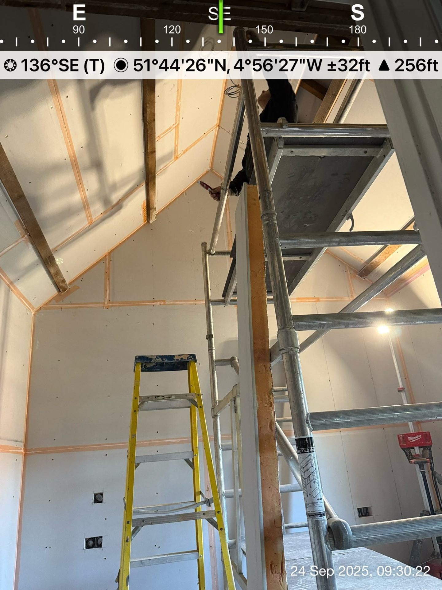 Plasterboard installation on a high vaulted ceiling with scaffolding and ladders in an interior room.