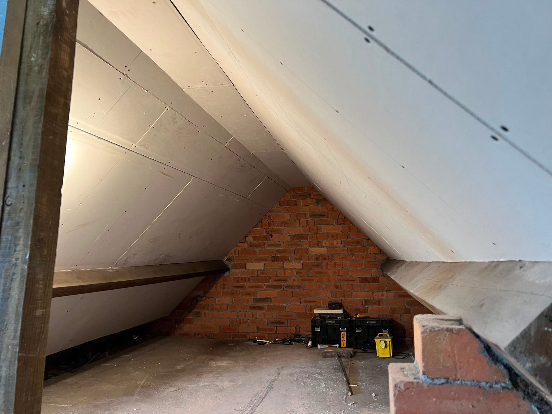 Inner loft space showing newly installed plasterboard sheets on sloped ceilings and exposed brickwork gable.