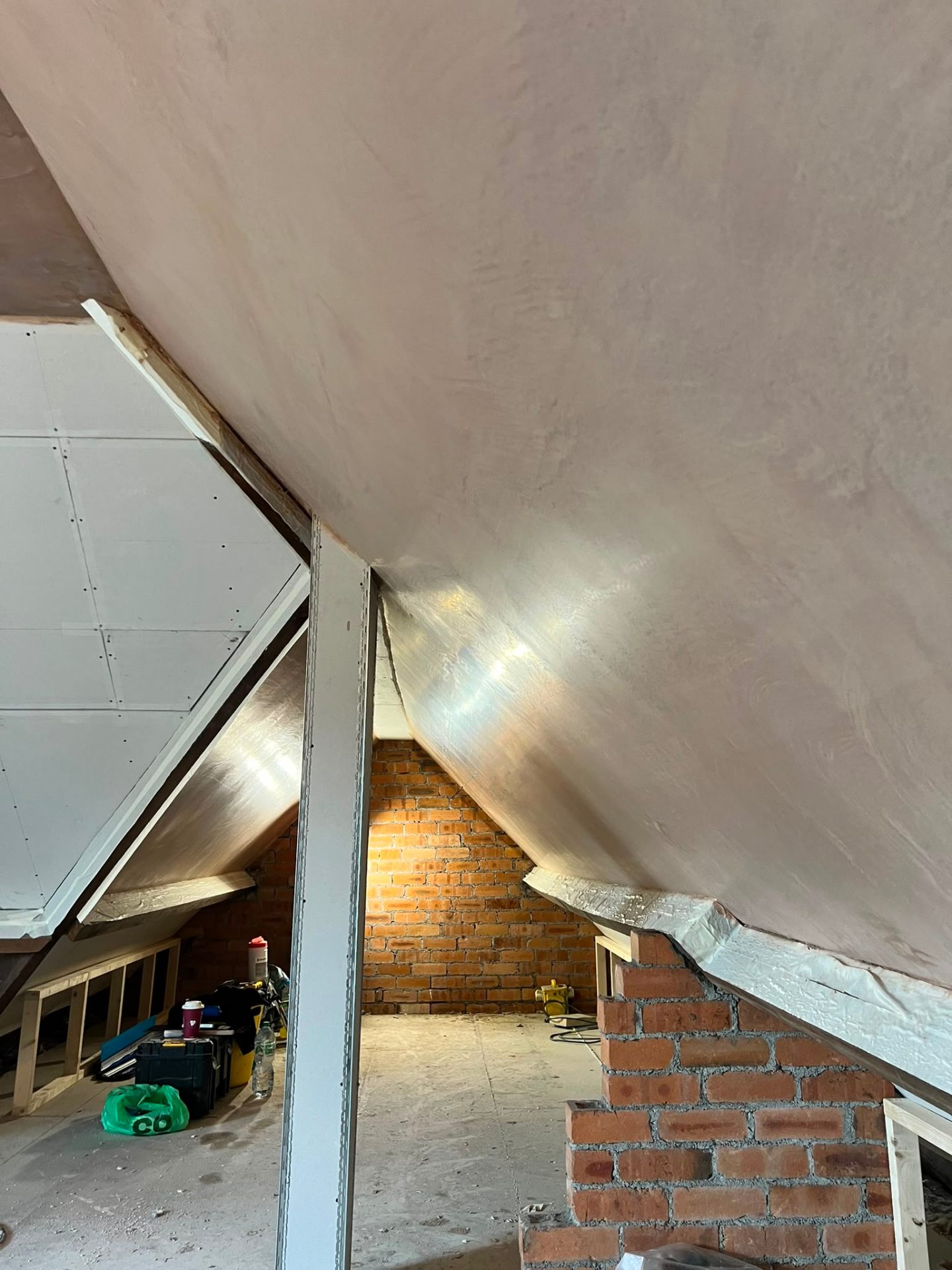 Wet plaster applied to a vaulted ceiling in a loft conversion next to exposed brickwork.