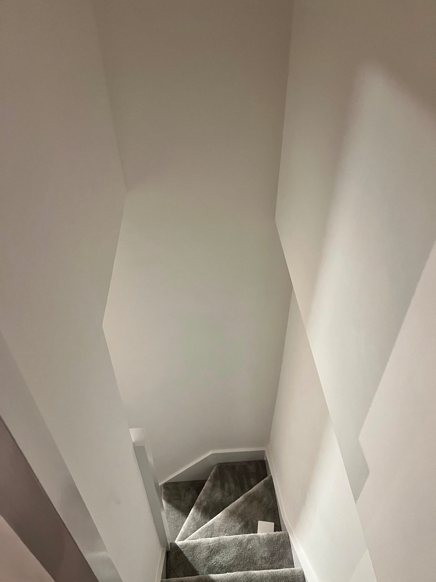 Top-down view of a freshly plastered white stairwell with grey carpeting installed.
