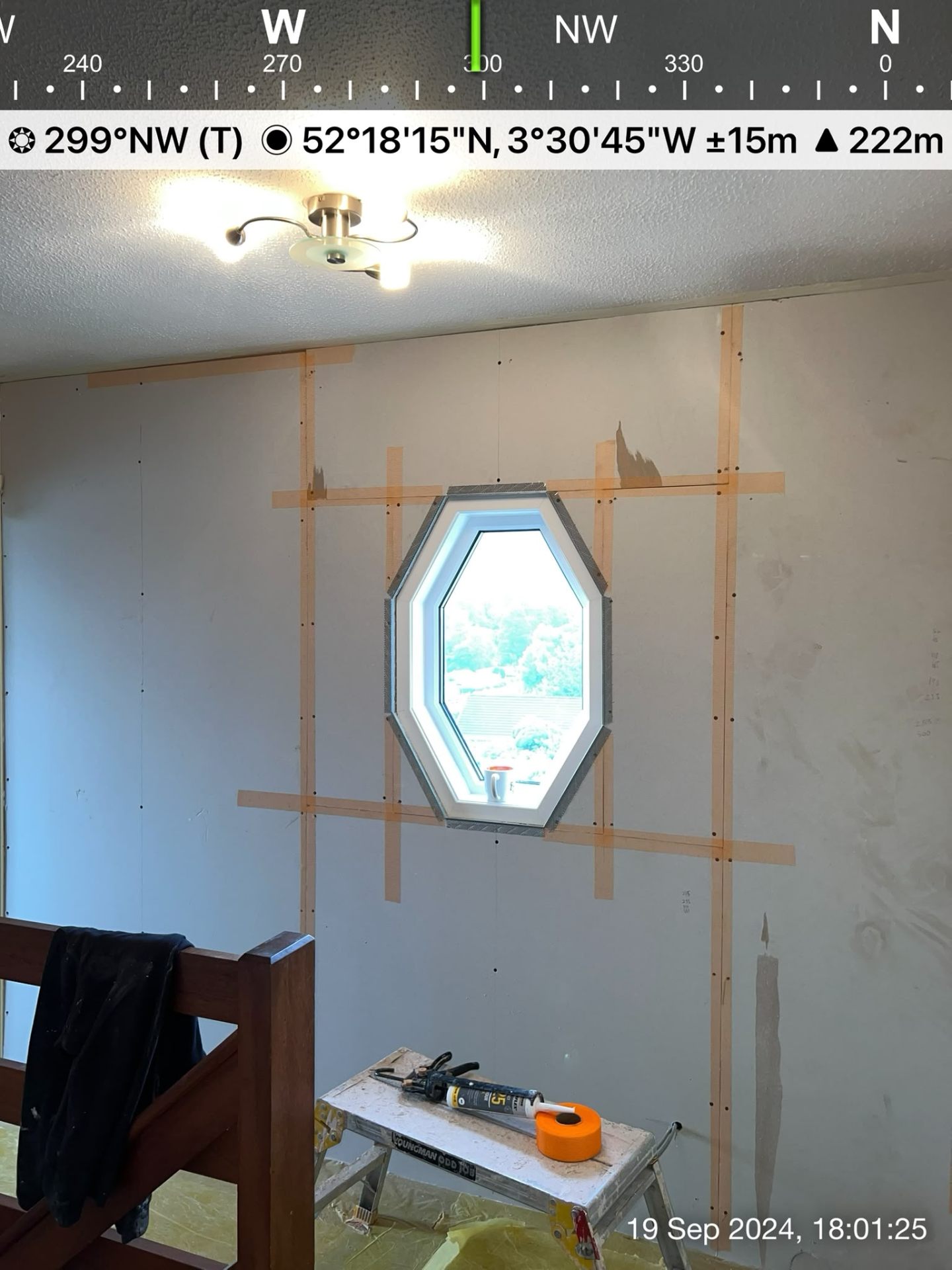 Large interior wall featuring drywall sheets and orange joint tape around a hexagonal window.
